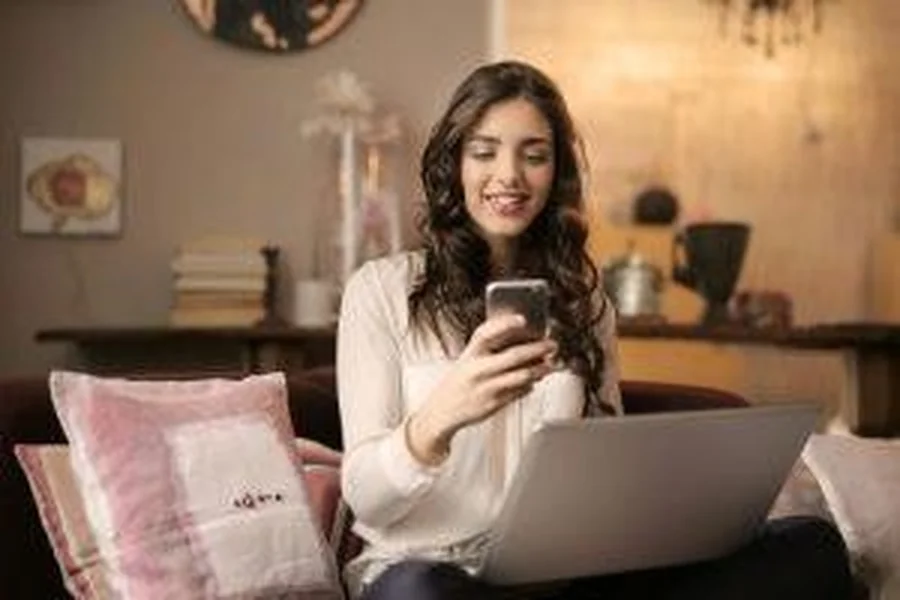 Woman smiling while using phone and laptop.